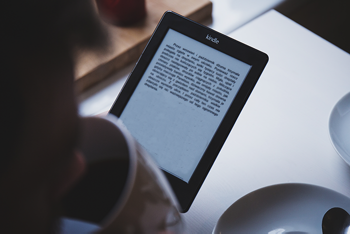 A person reading a Kindle Paperwhite while drinking a coffee